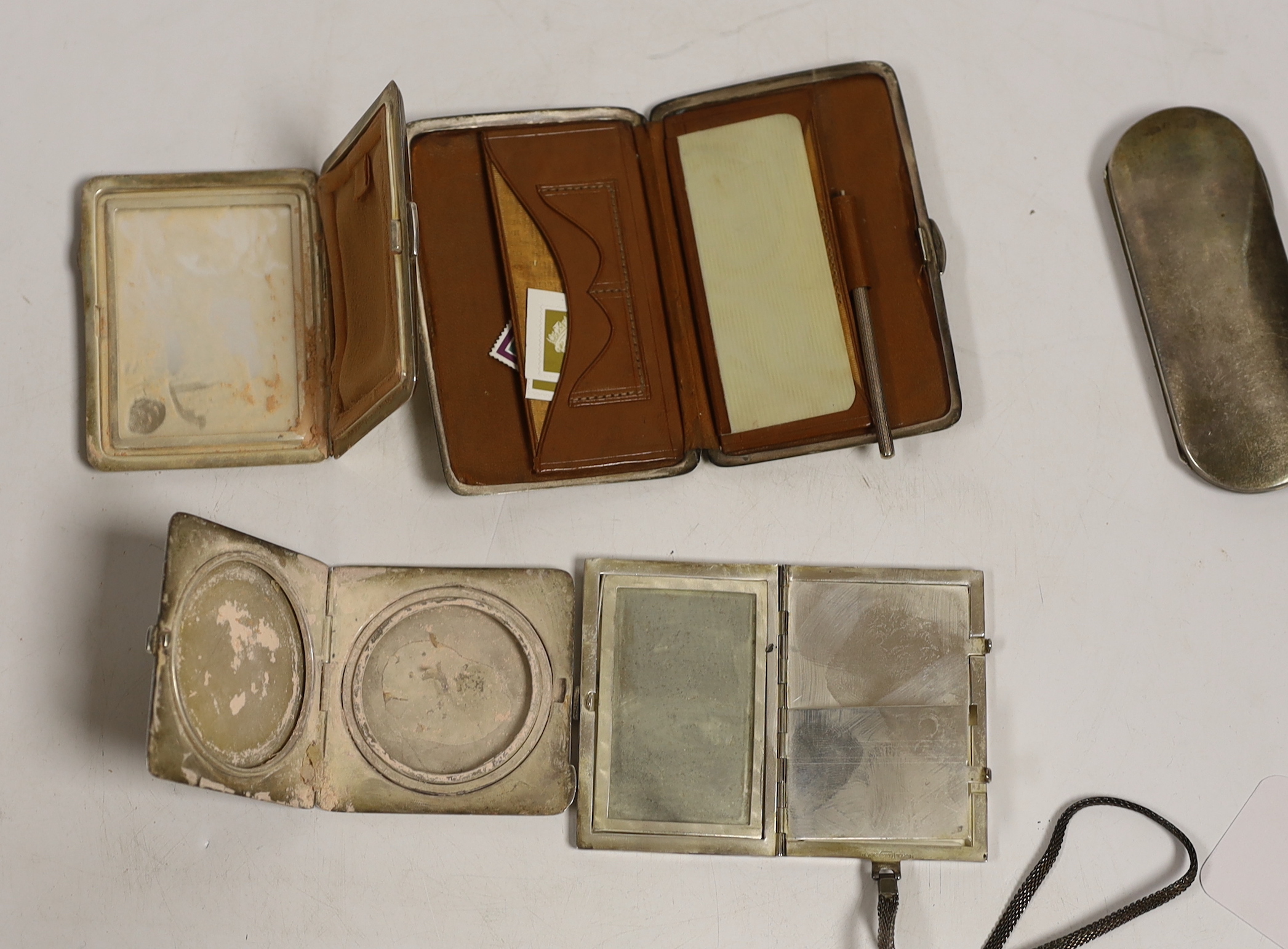 Two George V engine turned silver compacts, largest 83mm, a silver mounted aide memoire wallet, a silver spectacles case and a base metal compact.